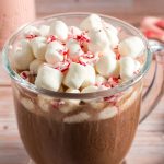 side view of hot chocolate in a glass cup topped with marshmallows and peppermint